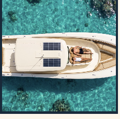 Aerial view of a private boat on clear turquoise water over coral, with two guests sunbathing on the bow lounge